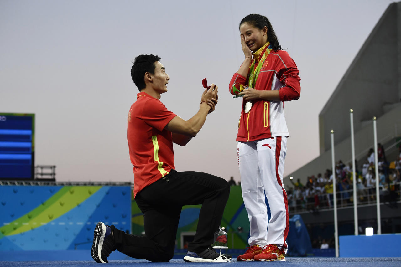Silver medallist China's He Zi (R), reacts she receives a marriage proposal from Chinese diver Qin Kai during the podium ceremony of the Women's diving 3m Springboard Final at the Rio 2016 Olympic Games at the Maria Lenk Aquatics Stadium in Rio de Janeiro on August 14, 2016. / AFP PHOTO / CHRISTOPHE SIMON